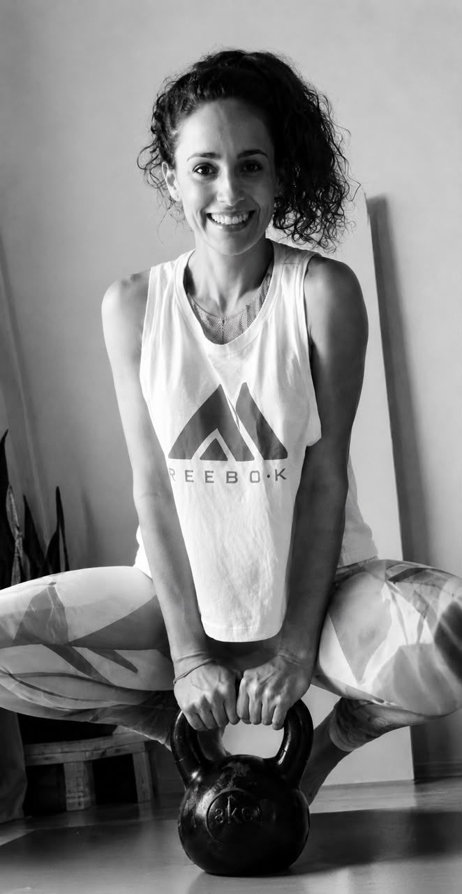 Paula sonriendo, en cuclillas con una pesa rusa apoyada delante